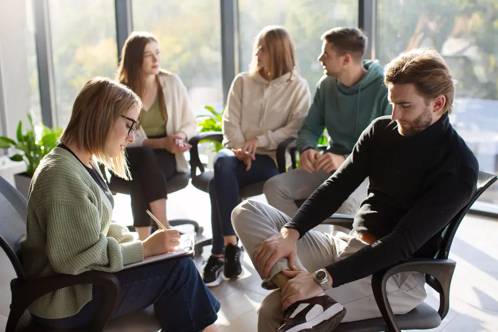 Group therapy session focused on recovery coaching, with individuals engaged in discussion and skill development in a bright, supportive environment.