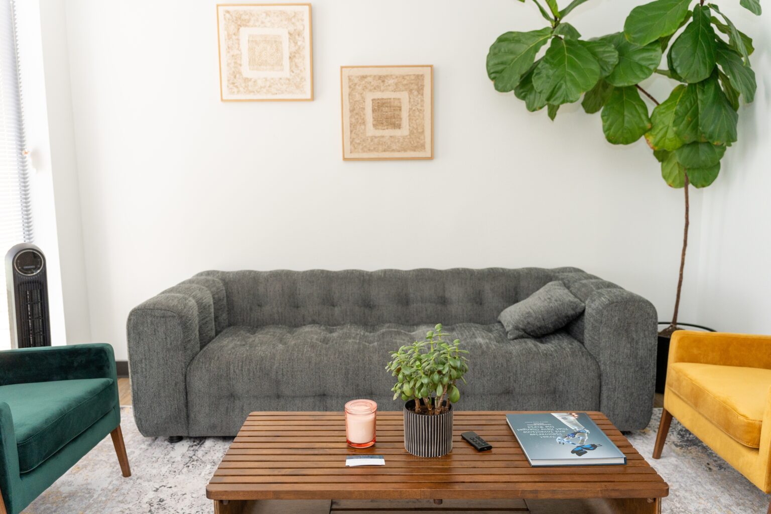 Cozy therapy room with a gray tufted couch, green and yellow chairs, a wooden coffee table with a plant, candle, and a book, designed for adult and teen recovery sessions.