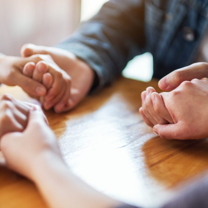 Group of people sitting in a circle holding hands and pray together or in therapy session