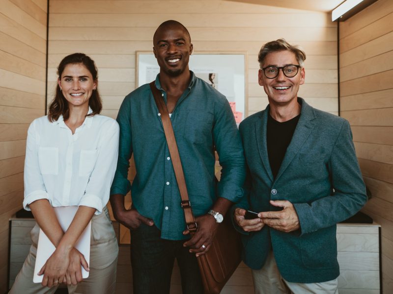 Group of diverse business professionals. Three multi-ethnic business people standing together in office looking at camera and smiling.