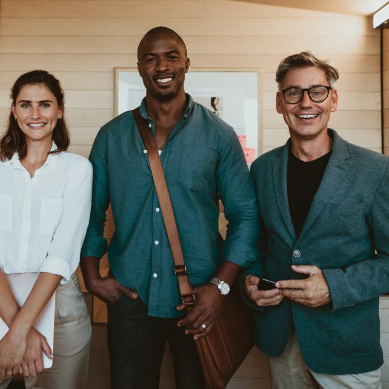 Group of diverse business professionals. Three multi-ethnic business people standing together in office looking at camera and smiling.