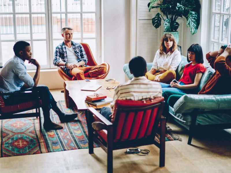 Group therapy session in a cozy room, featuring adults engaged in discussion, promoting mental health recovery and support at Altura Recovery's Intensive Outpatient Program.